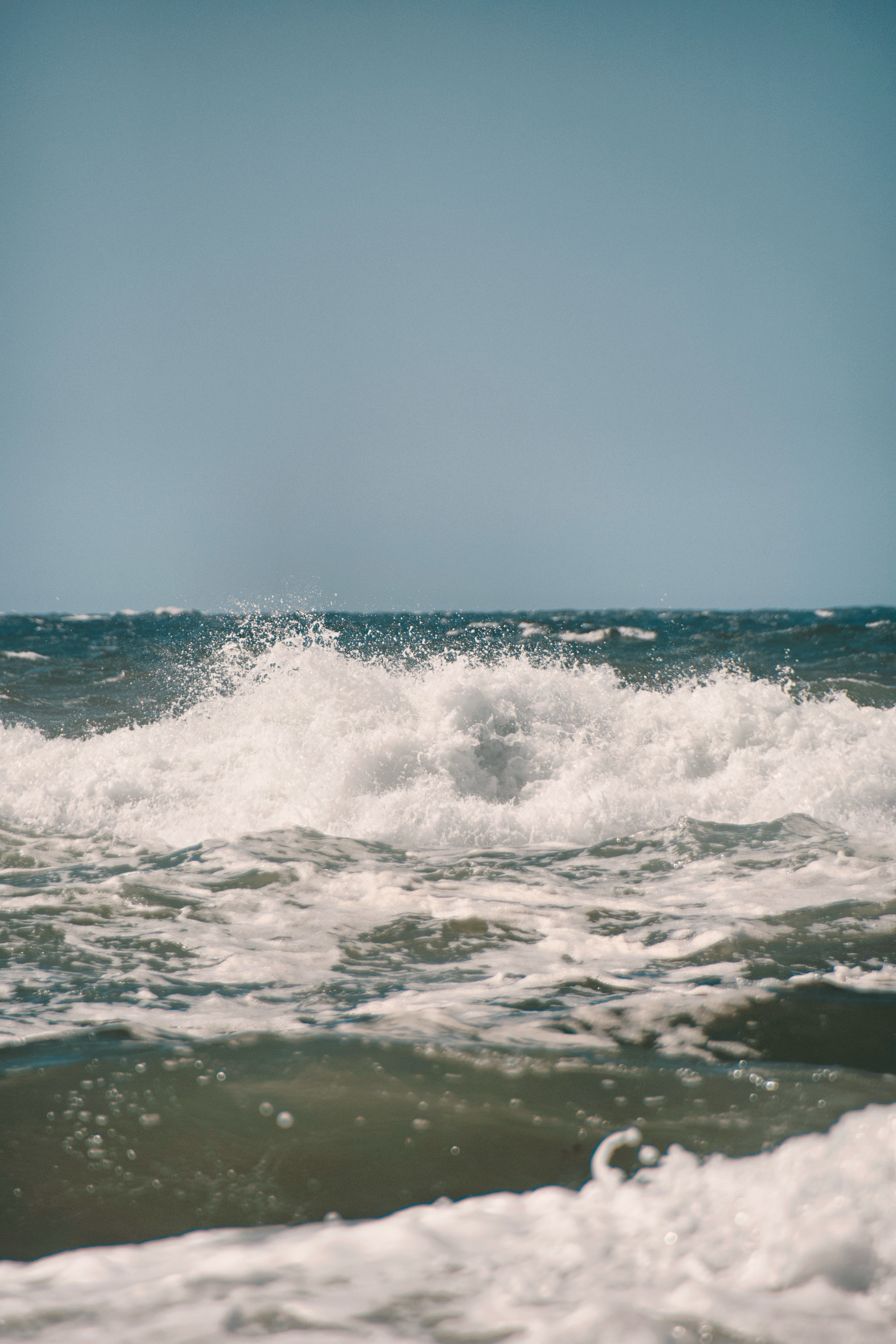Ocean waves crashing against the shore with a clear blue sky.