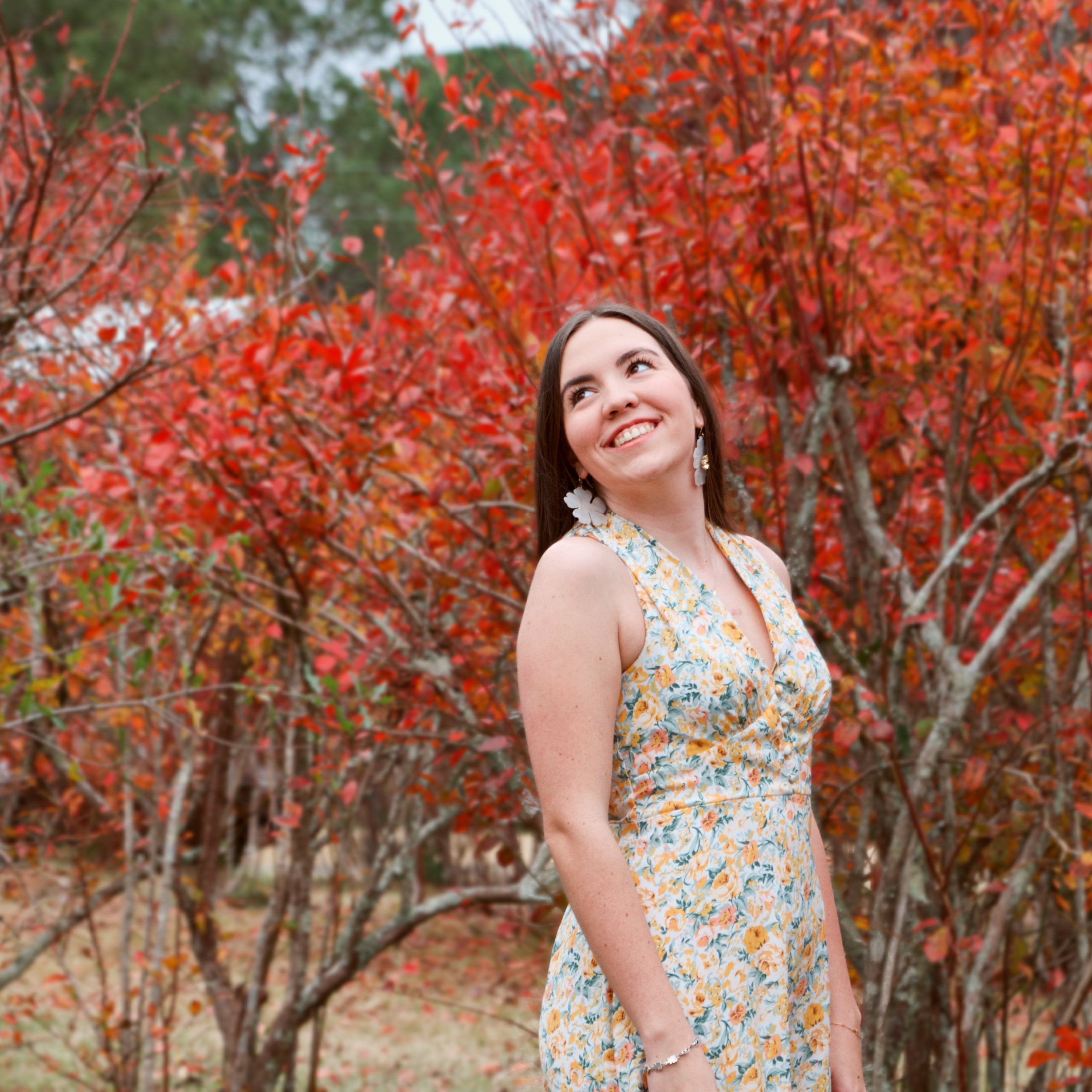 Woman in a floral dress standing in front of red autumn trees