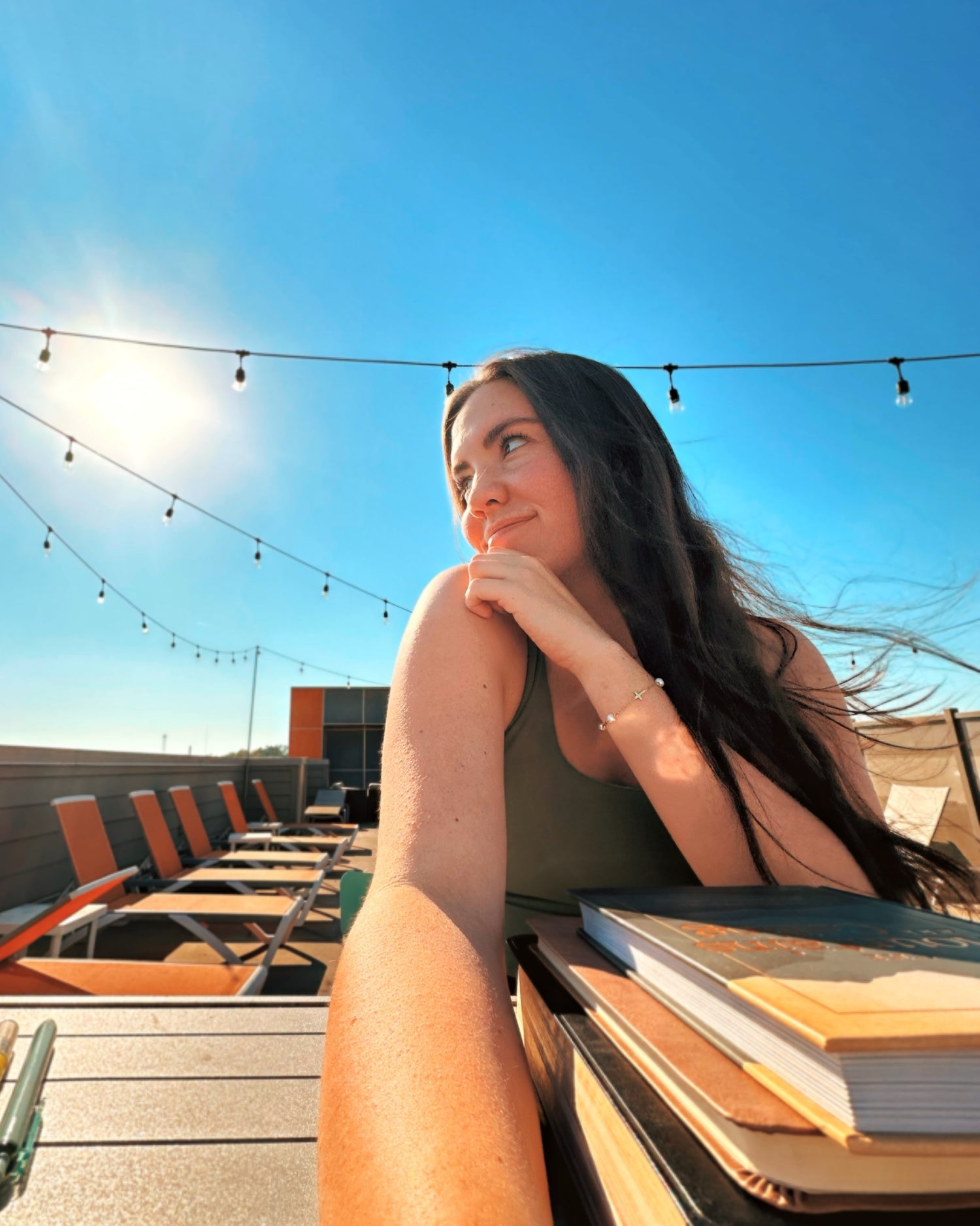 Woman sitting at a table, reading the Bible on a rooftop with a clear blue sky and string lights.